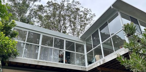 Modern house with large glass windows surrounded by trees.