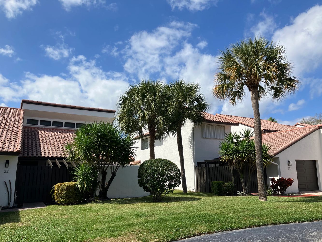 Sunny suburban homes with palm trees and green lawns under a blue sky.