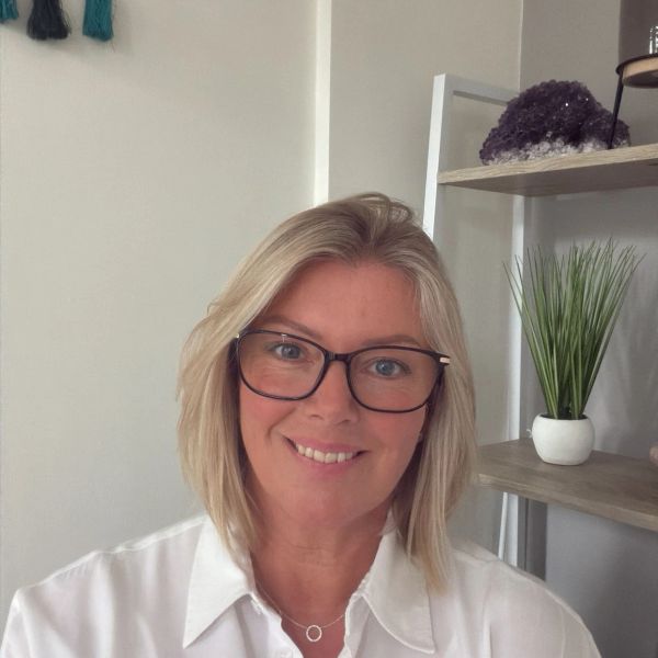 Smiling woman with glasses and blonde hair in a white shirt.