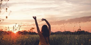 A silhouette of a young girl with her arms swayed above her head in crop field, a dusky sunset visib