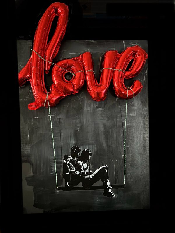 Red balloon letters spelling love with a couple sitting on a swing beneath.
