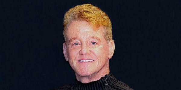 Smiling older man with light blond hair against a black background.