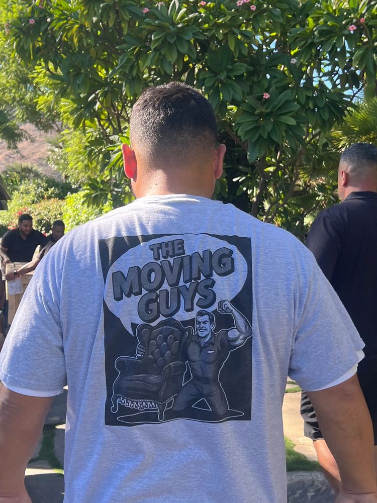 Man wearing a gray "The Moving Guys" t-shirt walking outside near a golf cart.