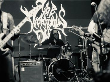 Black-and-white photo of a band performing live with a drummer center stage.