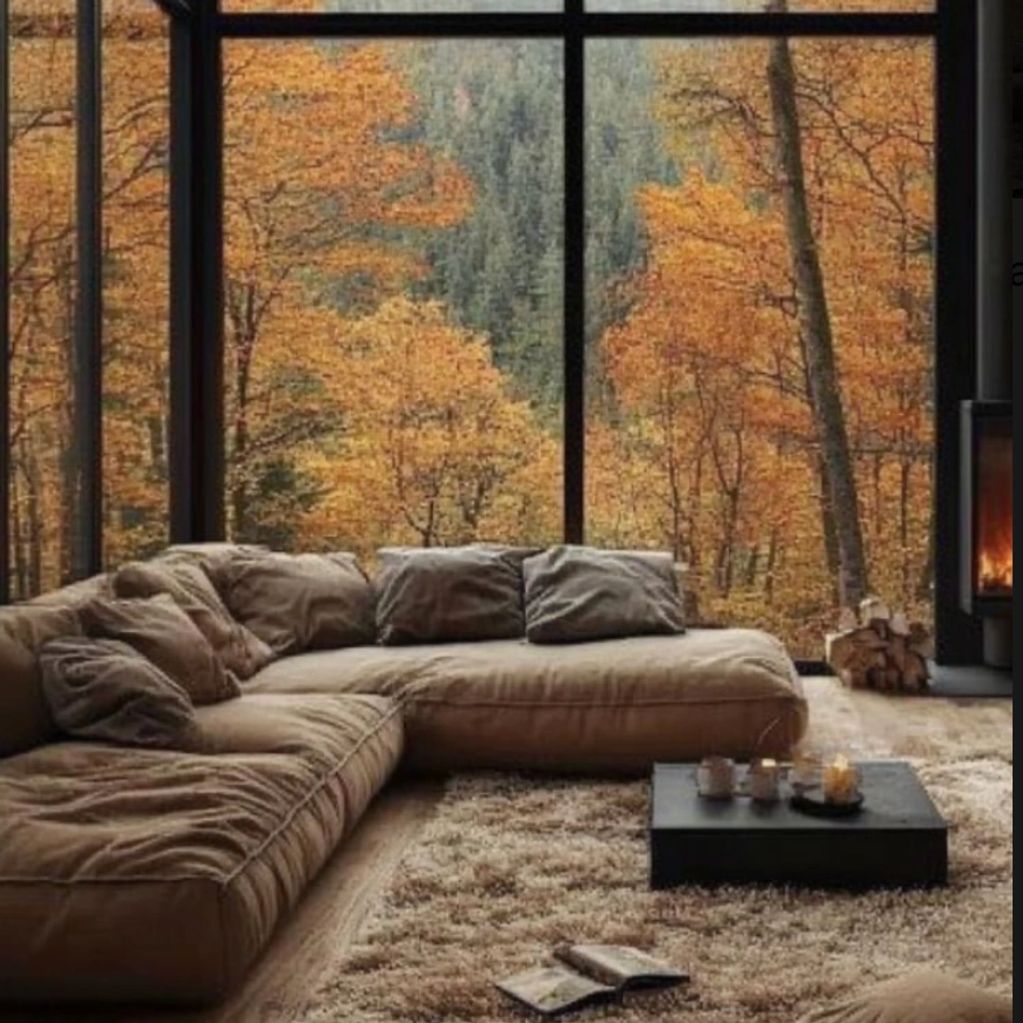 Cozy living room with a large window overlooking autumn forest scenery.