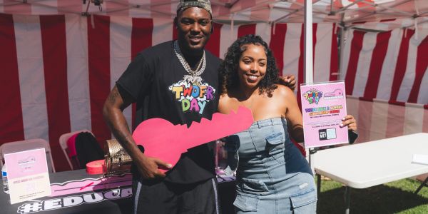Two smiling people holding a large pink key and a flyer under a red and white tent.