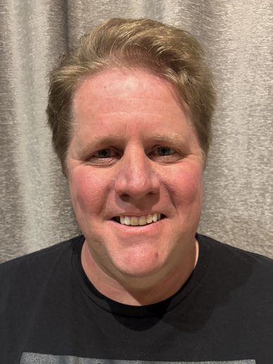 Smiling man with short, light brown hair wearing a black shirt.