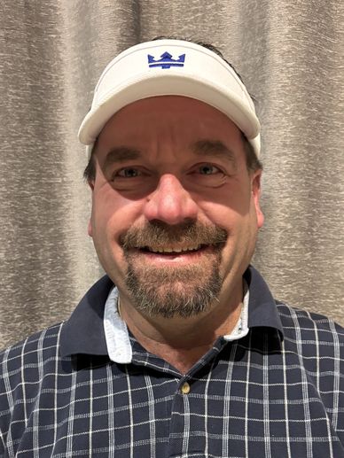 Smiling man in a checkered shirt and white visor standing indoors.
