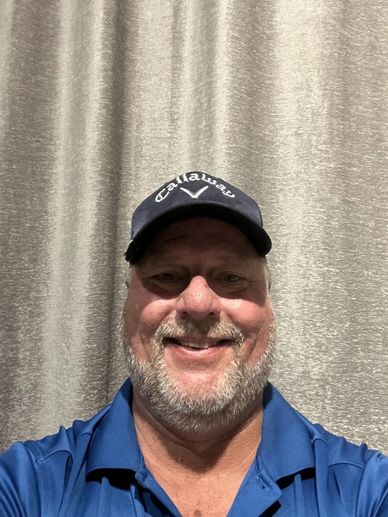 Smiling man in a blue shirt and Callaway cap against a gray curtain.