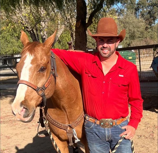 Man in cowboy attire standing with a horse outdoors.