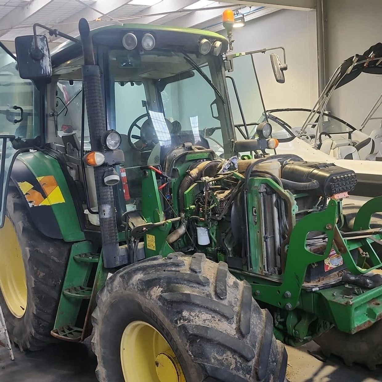 A green tractor with its hood open inside Tac Mechanical Ltd workshop, next to a boat and a ladder.