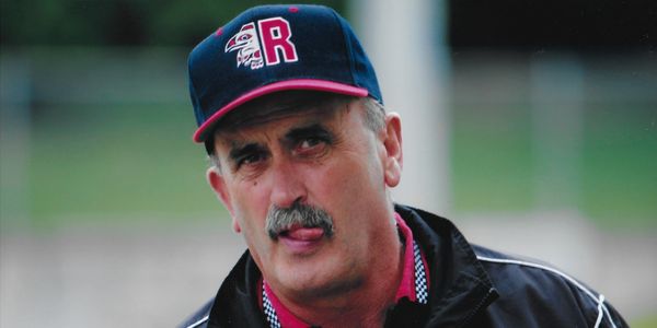 Man wearing a baseball cap and jacket sticking out his tongue.