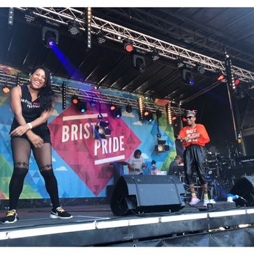 Mixed race interpreter smiling on stage at a Bristol Pride Event with a black female artist smiling 