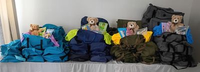 Four backpacks with teddy bears and supplies arranged on a table.