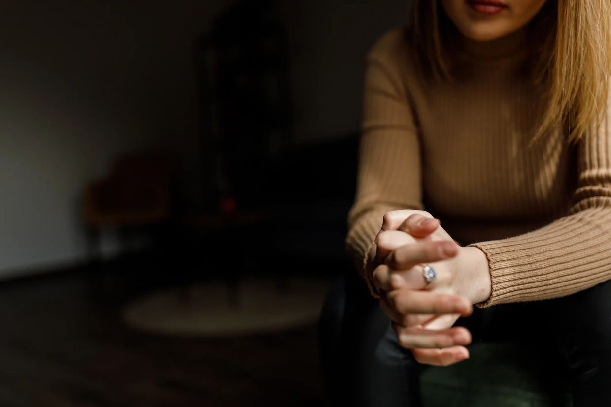 Mujer con suéter marrón entrelazando sus manos, parcialmente visible.