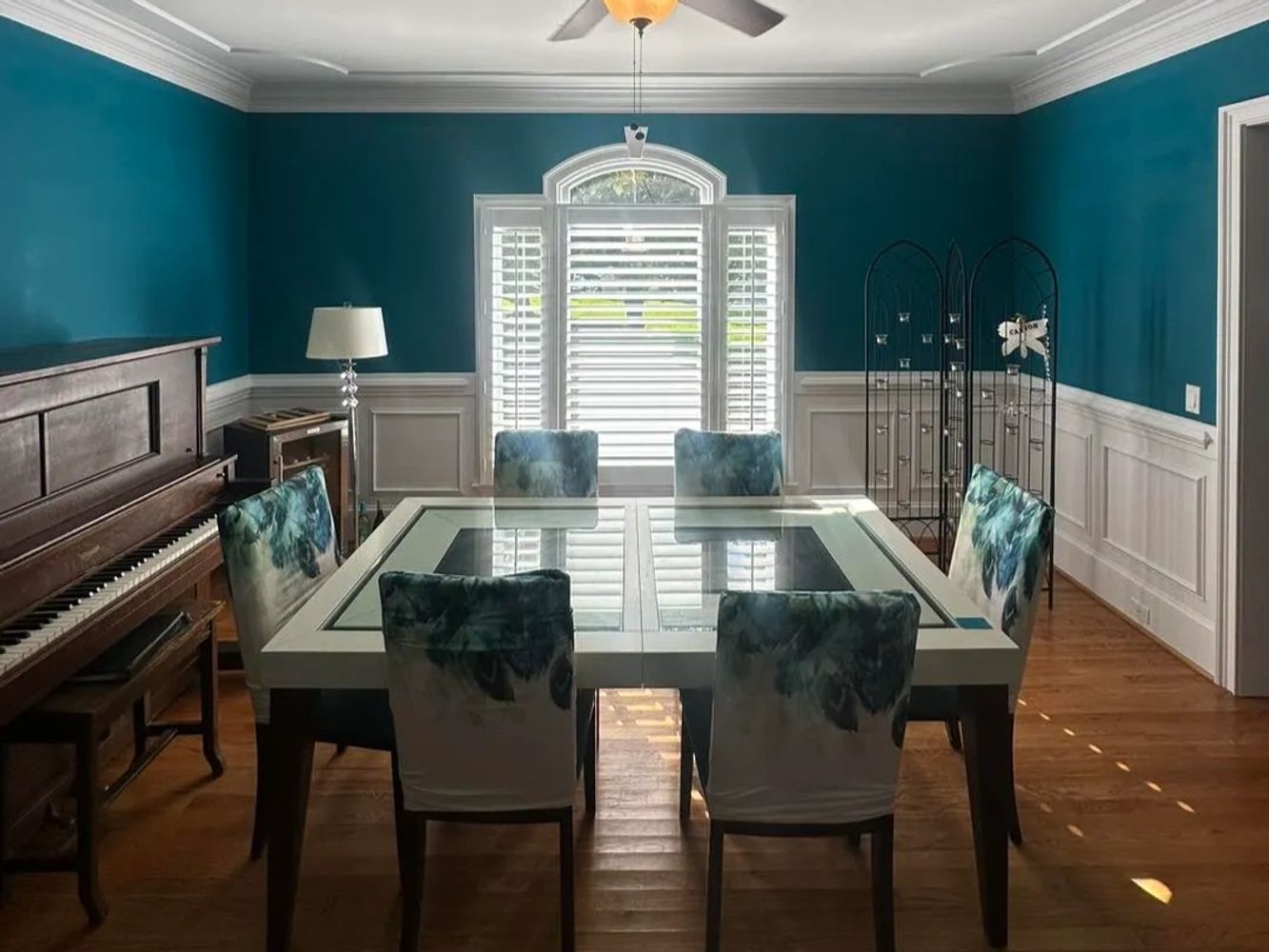 Teal dining room with white trim and a glass dining table
