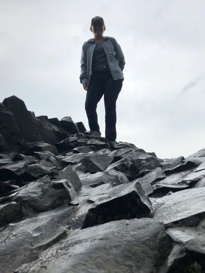 Person standing on jagged rocks against a cloudy sky.