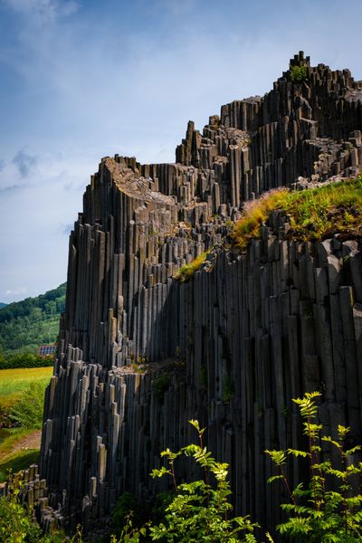 Columnar basalt rock formation under blue sky with greenery.