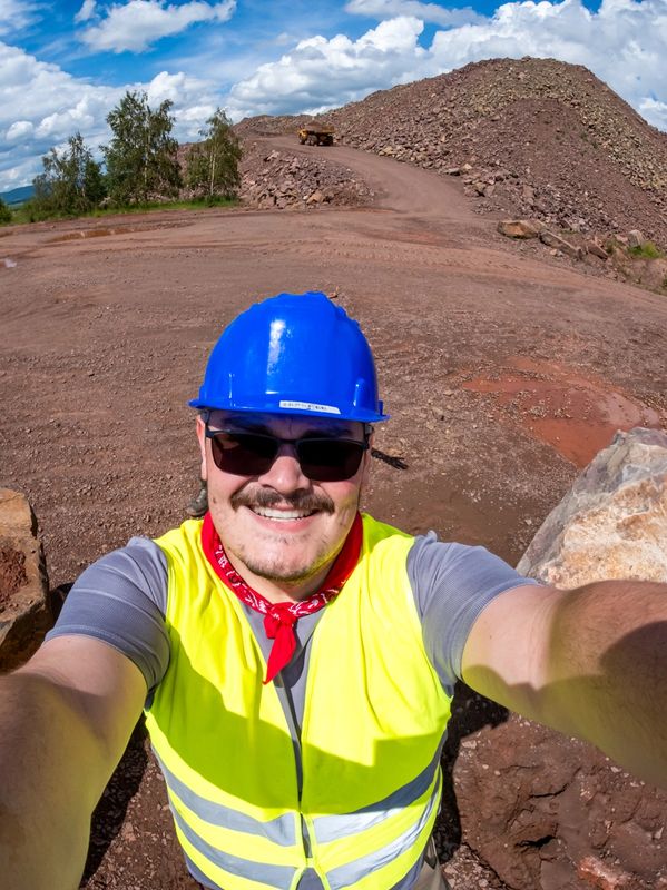 Smiling construction worker in safety gear takes a selfie at a rocky mining site.