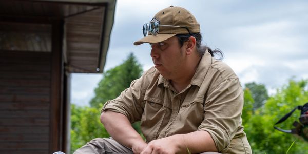 A man in outdoor attire sitting thoughtfully outside.