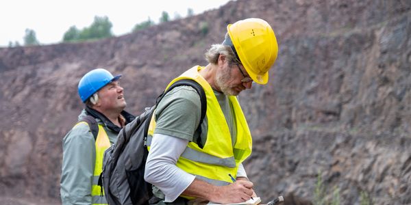 Two geologists in safety gear examining rock formations outdoors.