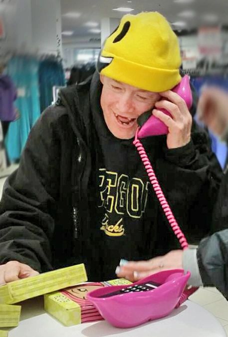 Smiling man wearing yellow hat pretending to talk on a lip-shaped telephone.