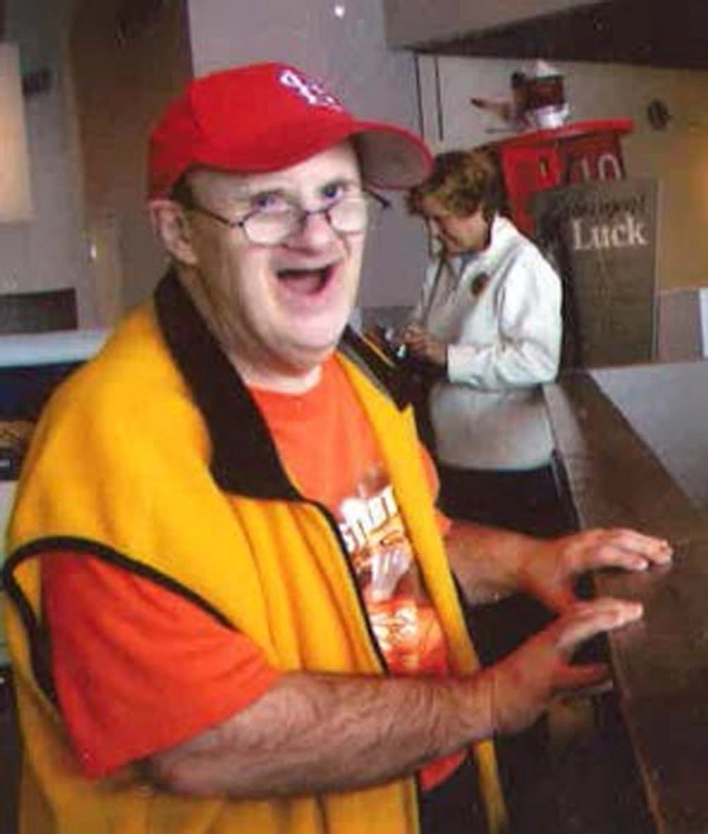 Smiling older man in a yellow vest at a counter.