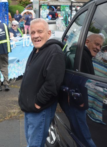 A smiling older man in a black hoodie leaning against a dark van