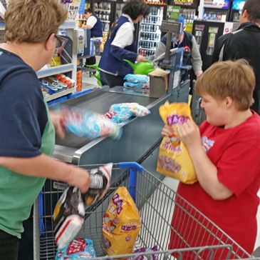 Two women loading items onto cash register checkout belt at grocery store.