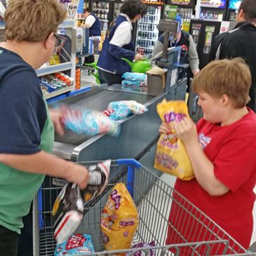 Two women loading items onto cash register checkout belt at grocery store.