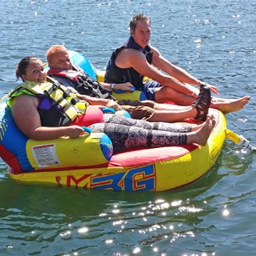 Three people in life jackets on float tubes on water.