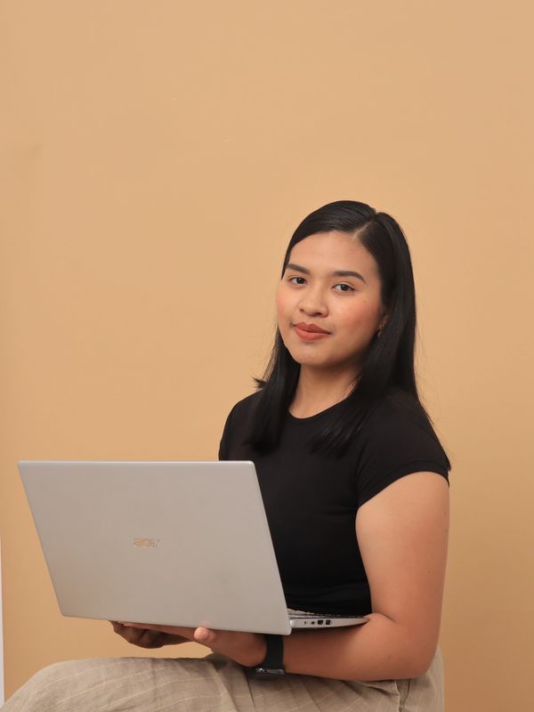 Young woman holding a laptop, posing confidently against a beige background.