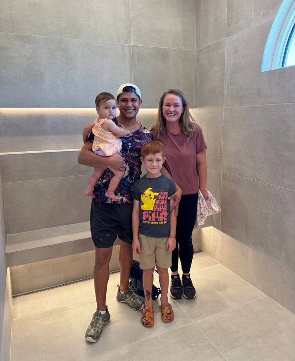Happy family of four posing indoors against a tiled wall.