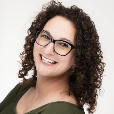 Smiling woman with curly hair and glasses against a white background.