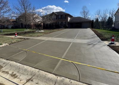 Newly poured concrete driveway with measuring tape and traffic cones.