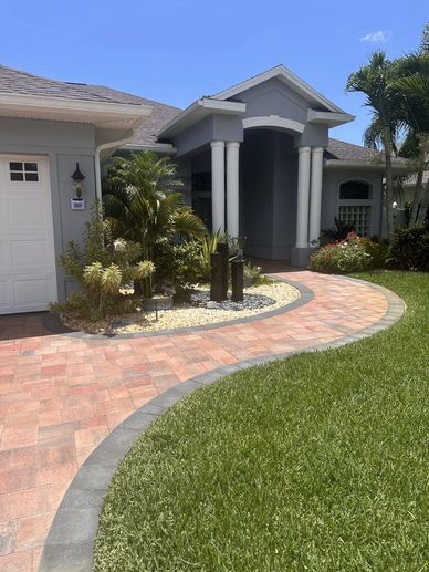 Curved brick pathway leading to a house porch with columns and greenery.