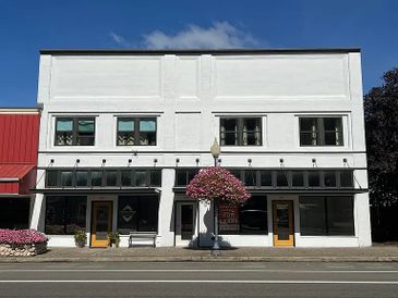 A white two-story building with yellow doors and a hanging flower basket outside.