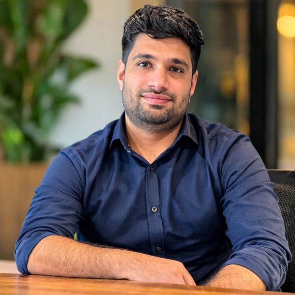 Man in navy blue shirt sitting at a wooden table, smiling gently.