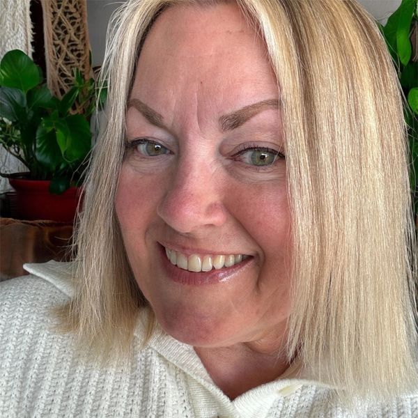 Smiling woman with blonde hair and green eyes in a cozy white sweater.