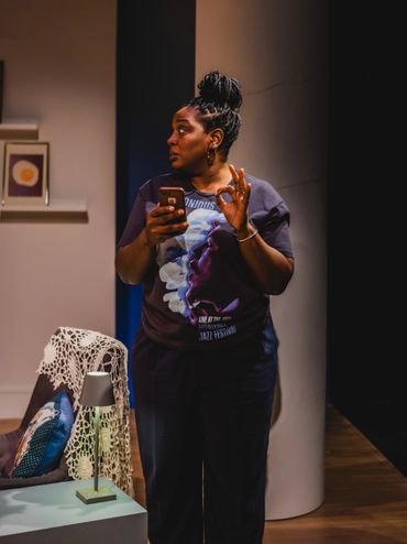 Woman with braided hair holding a phone and making an OK gesture indoors.