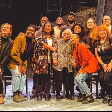 A joyful diverse group posing together on stage, smiling warmly.