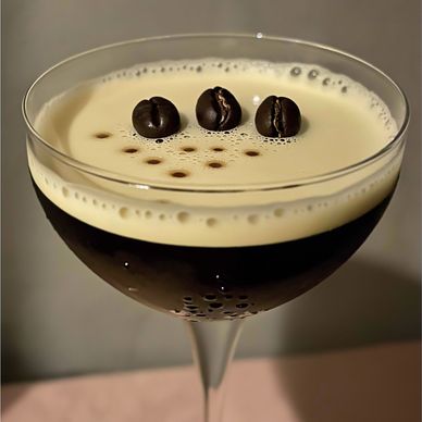 espresso martini in a coupe glass with 3 beans floating in glass