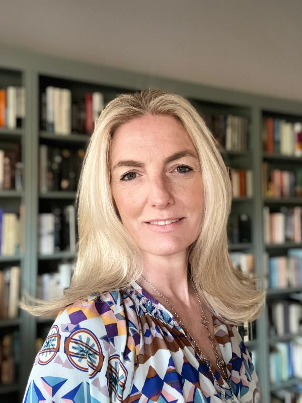 Blonde woman smiling with bookshelves in the background.