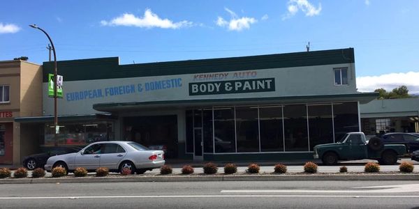 Auto body and paint shop with classic cars parked outside on a sunny day.
