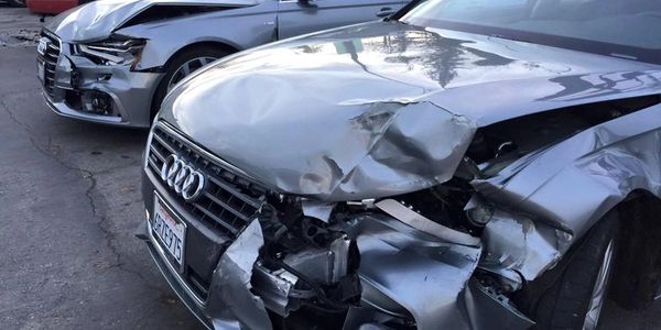 Two silver Audi cars with severe front-end collision damage.