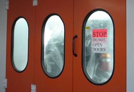 Orange doors with oval windows and a warning sign not to open them.