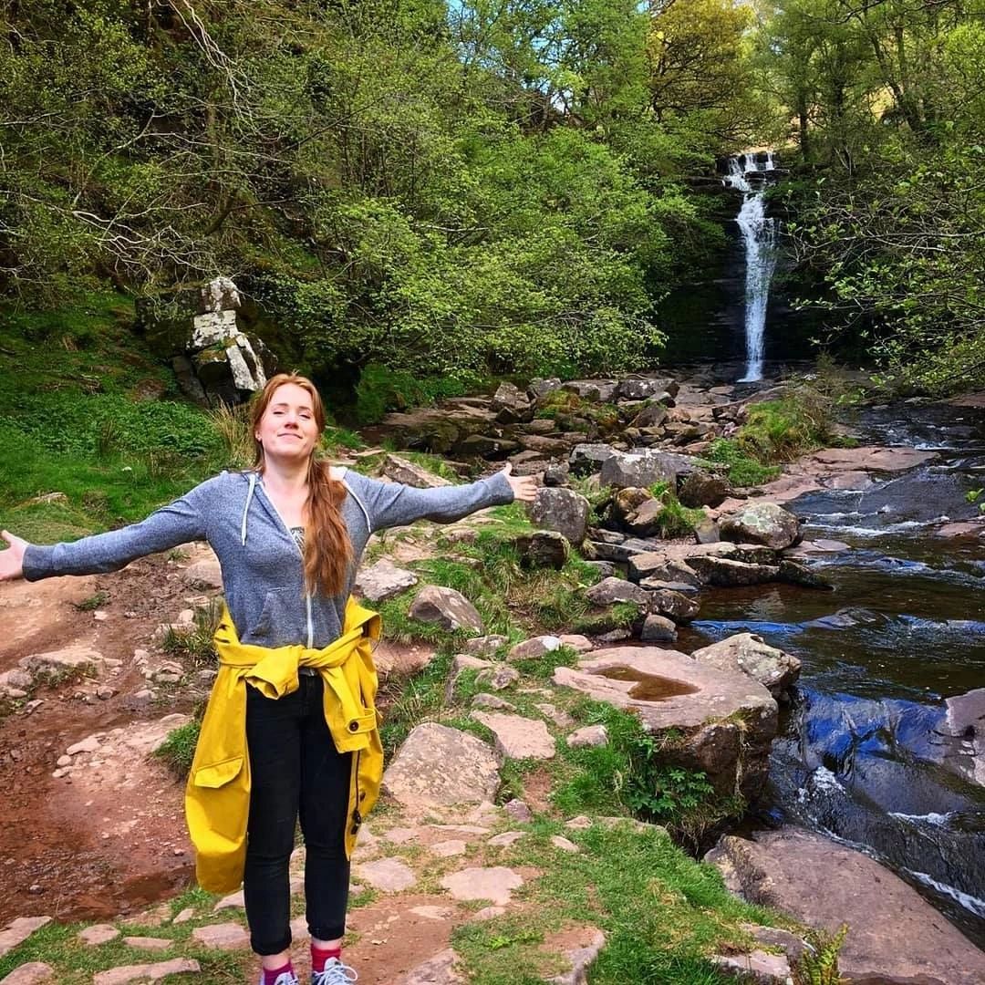 Harriet standing triumphantly in front of a small waterfall in Talybont-in-Usk 