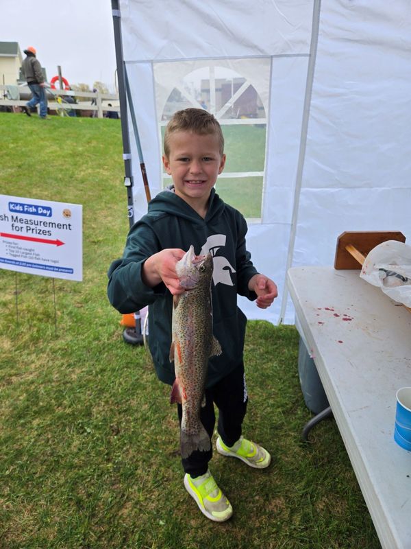 A boy proudly holds a large fish at a kids' fishing event.