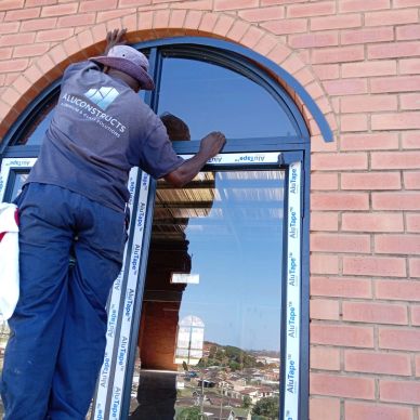 Worker installing an arched window on a brick building.