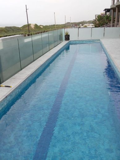 Long outdoor swimming pool with glass fencing.